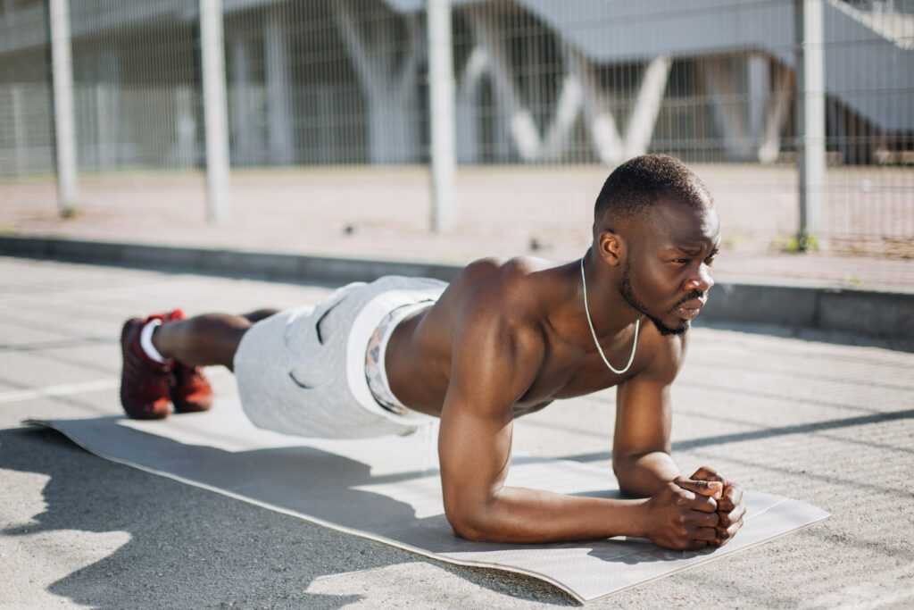 African American man stands on his arms on the ground doing plank exercises